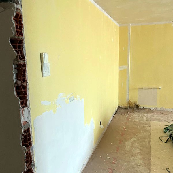 Pared antigua con gotelé siendo cubierta por placas de yeso laminado lisas en una reforma en Alzira.