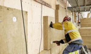 Operario instalando paneles de lana de roca para aislamiento térmico en un trasdosado de yeso laminado.
